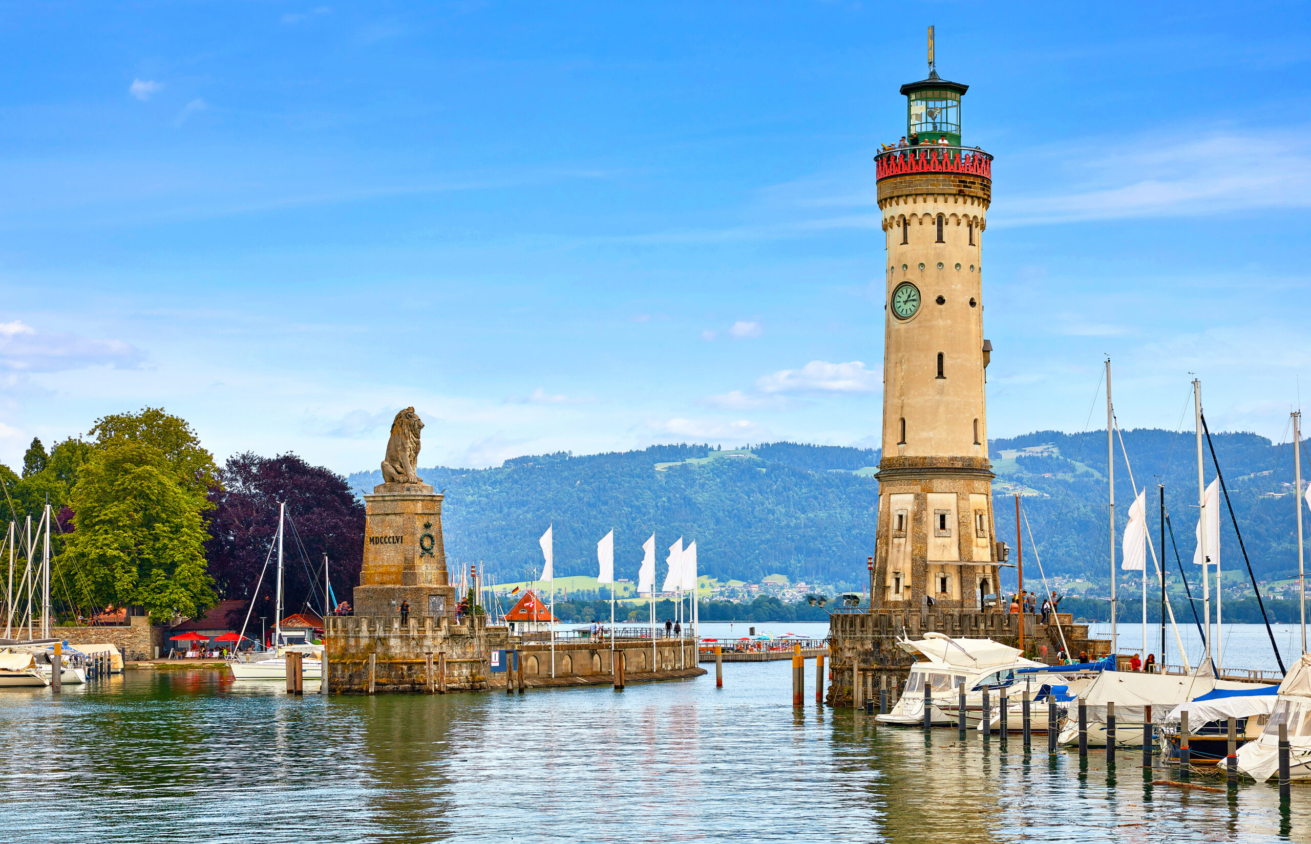 Hafeneinfahrt von Lindau am Bodensee mit historischem Leuchtturm und Löwenstatue vor Alpenpanorama.